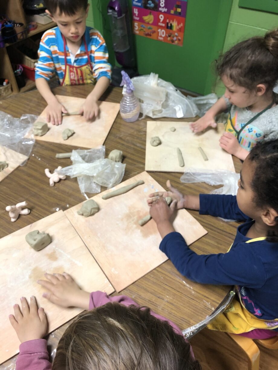 Children shaping clay on wooden boards in a classroom.