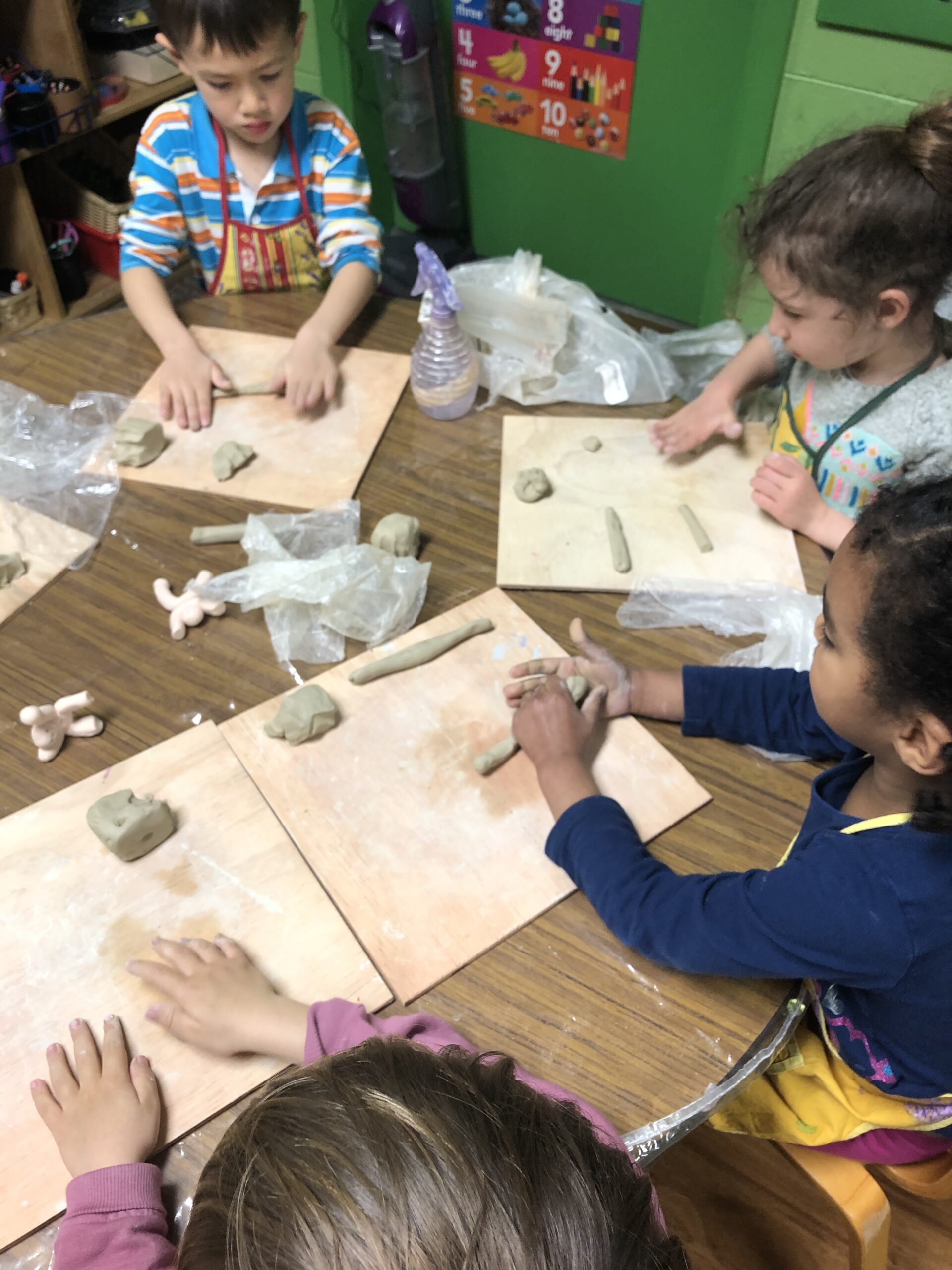 Children shaping clay on wooden boards in a classroom.