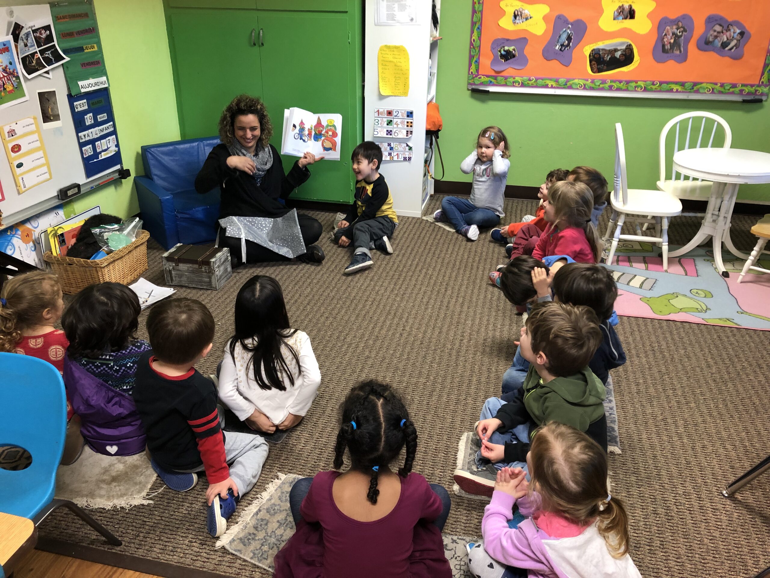 Teacher reading a book to a group of young children in a colorful classroom.