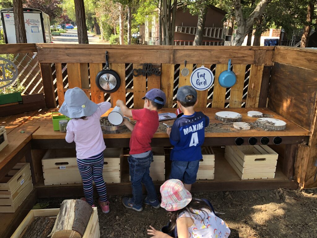 Children play with wooden toys at an outdoor activity table.