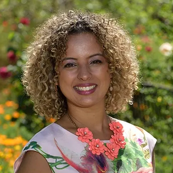 Smiling woman with curly hair in a floral dress outdoors.